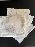 Stacked tablecloth and napkins showing scalloped edges and embroidery