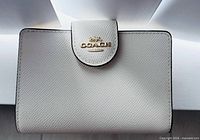 Front view showing off-white pebbled leather and gold-tone Coach logo plaque