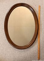 Front view of oval wood-framed mirror with ruler for scale
