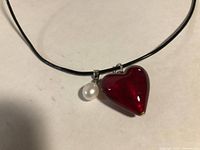 Close up of necklace showing black cord, white pearl pendant, red glass heart pendant