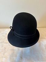 Front view of black felt cloche hat showing shape and ribbon bow