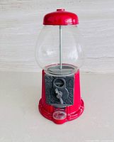 Front view showing red metal base, glass globe, coin mechanism with key, and plastic tray