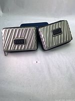 Two silver hard-shell cases with blue pouch behind