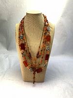 Front view showing all three layered orange-tone necklaces on bust