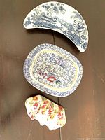 Three items laid out: top crescent blue transfer dish, middle rectangular blue transfer dish, bottom floral chintz toast rack