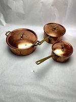 Three copper saucepans with lids displayed