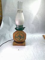 Front view of lamp showing wood base, green metal collar, frosted globe, clear chimney, cord and plug