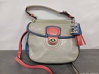 Front view showing color block design, top handle, crossbody strap, turn-lock closure, hangtag and tassel