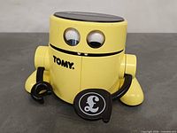 Front view showing Tomy logo, eyes, arms, coin tray