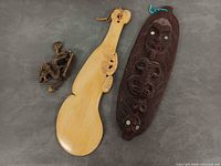 Group shot of all three items: brass dragon, pale wood club, dark waka huia lid