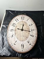 Front view of oval wall clock showing dial, numerals, hands