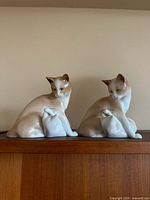 Two identical Siamese cat and kitten figurines on wooden surface