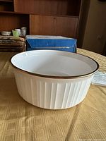 Round white fluted dish with gold rim on table, leaflet visible