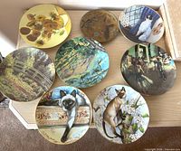 Eight assorted round plates on dresser including sunflower, cats, landscapes