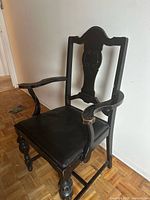Left front angle view of black wooden armchair showing seat, arms, legs