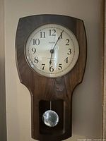 Front view of Bulova wooden wall clock showing dial and pendulum