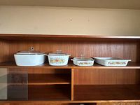 Four CorningWare pieces lined on shelf with lids visible