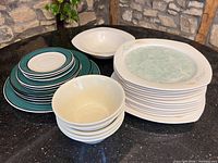 Group view of stacked square plates, teal-rim plates, cereal bowls and serving bowls
