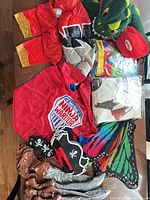 Overall view of loose costume items including Mario cap, pirate hats, Ninja Warrior pieces, dinosaur hood, butterfly wings, inflatable props