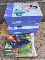 Two boxed Aerobed Over-Nighter mattresses stacked above opened Ozark Trail twin airbed box