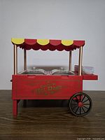 Front view of red Nostalgia HDM503 hot dog cart showing canopy, lids, wheel