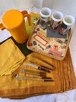 Group shot of all items: placemats, pitcher, tumblers, tray, utensils, napkins, tea towel