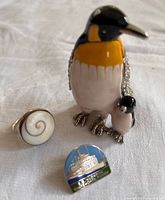 Front view of penguin trinket, shell ring and enamel pin