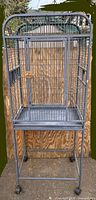 Full view of tall grey metal bird cage on wheeled stand