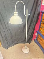 Full view of white metal floor lamp with curved arm and dome shade