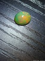 Oval cabochon opal on textured background showing green and orange pinfire