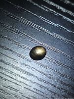 Oval black star sapphire on dark textured surface, star effect visible
