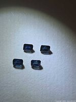 Four loose emerald-cut blue sapphires on neutral background