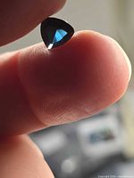 Trillion cut deep blue spinel held between fingertips
