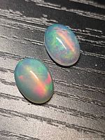 Two oval crystal opals showing colour play on dark surface