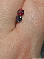 Pair of loose cushion-cut spinels on fingertip showing size and colors