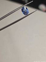 Oval cornflower blue sapphire held by tweezers, side view