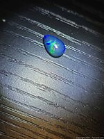 Pear-shaped Ethiopian black opal on dark surface showing blue and green play-of-color