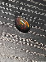 Oval Ethiopian black opal showing multicolour play on dark surface