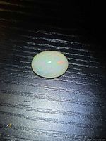 Loose oval opal cabochon showing play-of-colour on dark surface