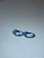 Two oval faceted sky blue topaz stones on neutral background