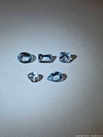 Five mixed-cut light blue aquamarines on neutral background