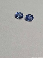 Two oval cornflower blue sapphires on neutral background