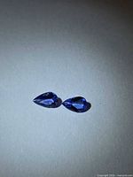 pair of pear-cut deep blue-violet Tanzanite gemstones on neutral background