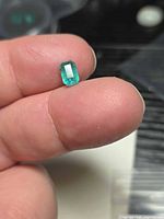 Octagon-cut emerald held between fingers showing face-up color and clarity