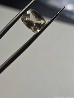 Cushion-cut beryl held by tweezers, showing transparency and pale yellow tone
