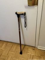 Full view of the brown adjustable Airgo cane leaning against wall