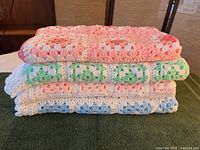 Stacked view of three folded crocheted blankets showing colour variations