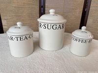 Front view of three white ceramic canisters with lids