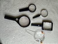 Six magnifying glasses laid out to show variety in size, shape and handles