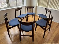 Six mid-century chairs arranged in circle showing curved backs and blue seats